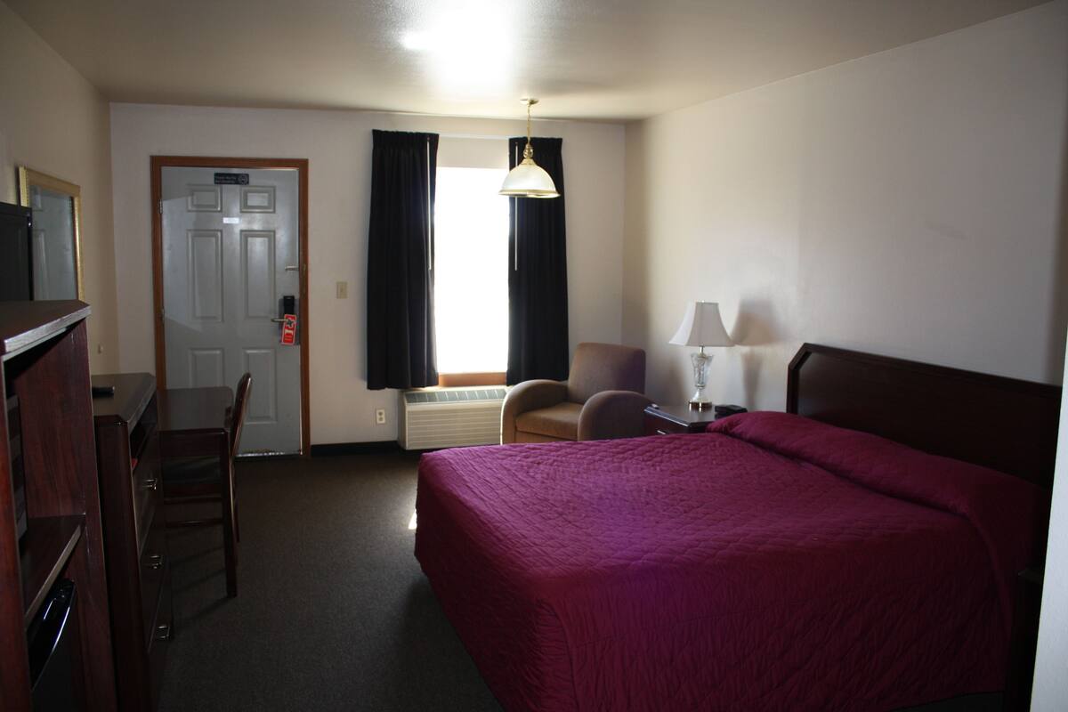 A hotel room with a bed, a desk, a chair, a lamp, and a window with curtains.