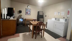 A small kitchenette with a refrigerator, microwave, and coffee maker. There is a wooden table with chairs and a clock on the wall. - Boomtown Inn (Drumright)