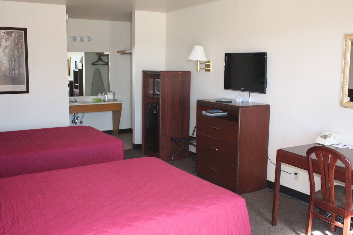 A hotel room with two beds, a desk with a chair, a television, a telephone, and a mirror.