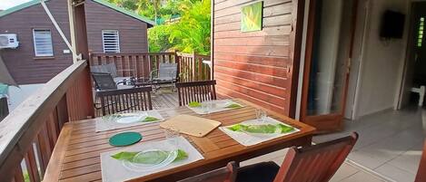 Una terraza de madera con una mesa lista para dos, sillas y una lámpara colgante.