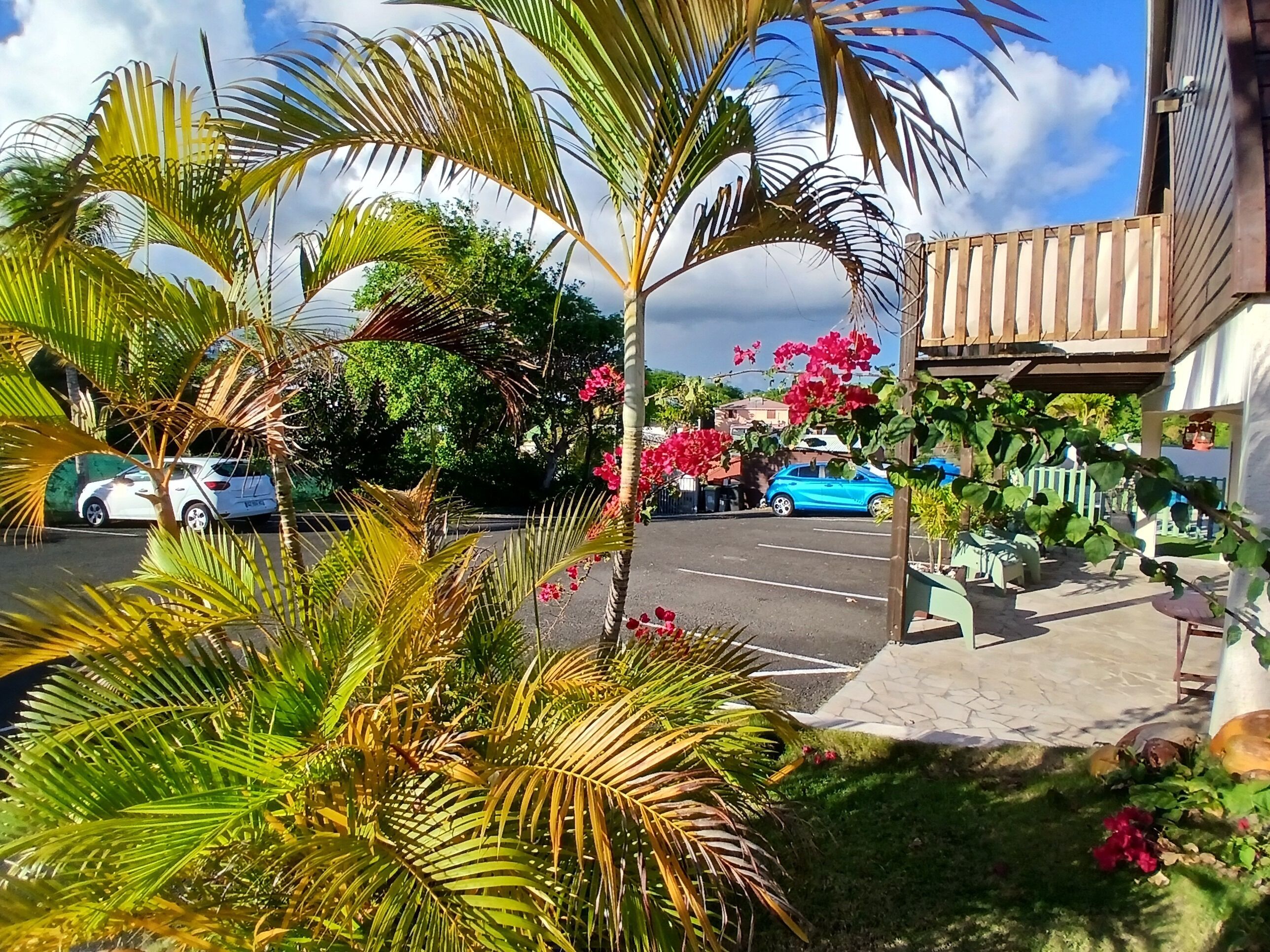 Un estacionamiento con coches, un edificio con balcón de madera y abundante vegetación.