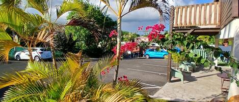 Un estacionamiento con coches, un edificio con balcón de madera y abundante vegetación.