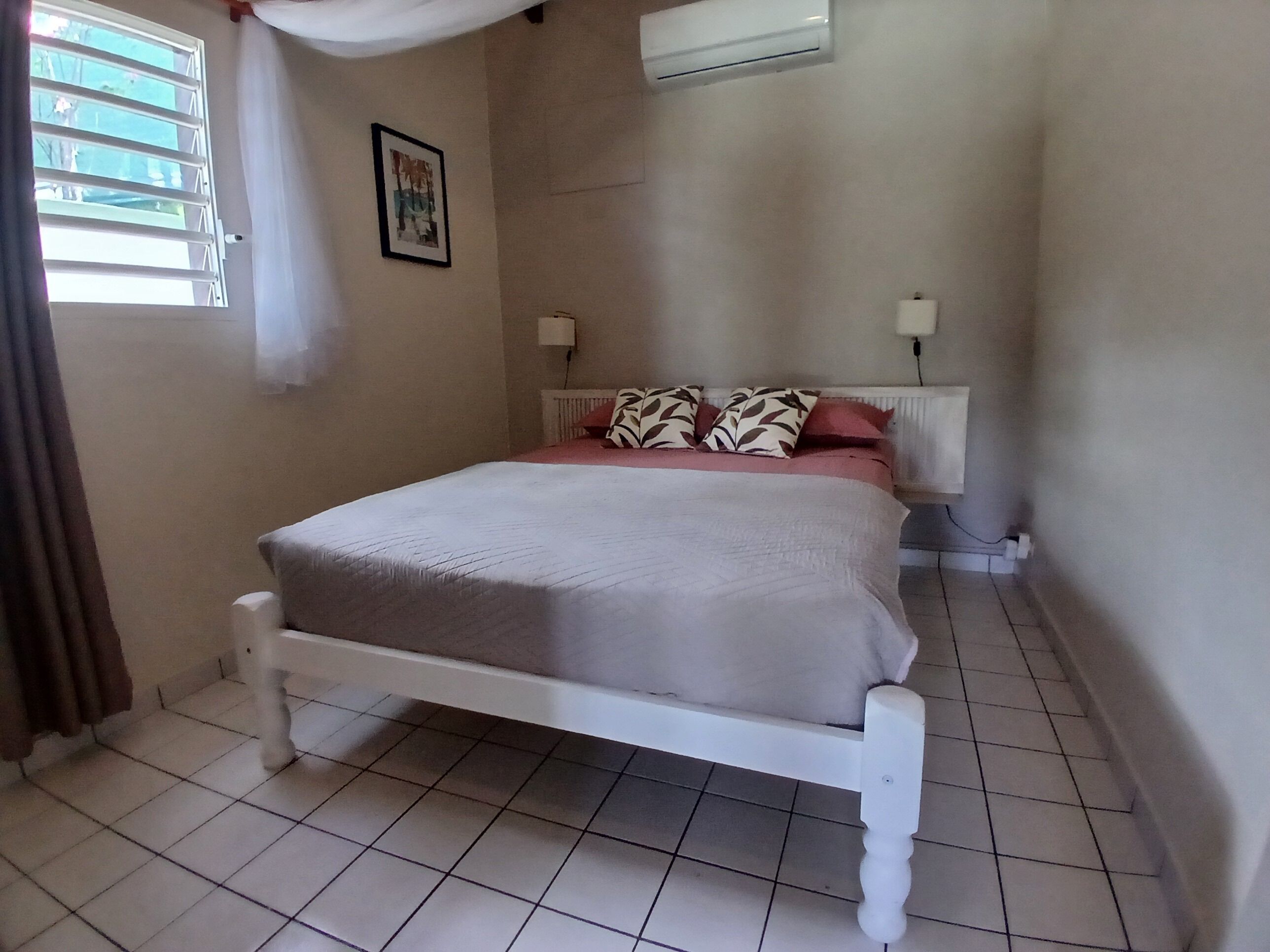 A bedroom with a bed, a window with curtains, a radiator, and a wall-mounted air conditioner.