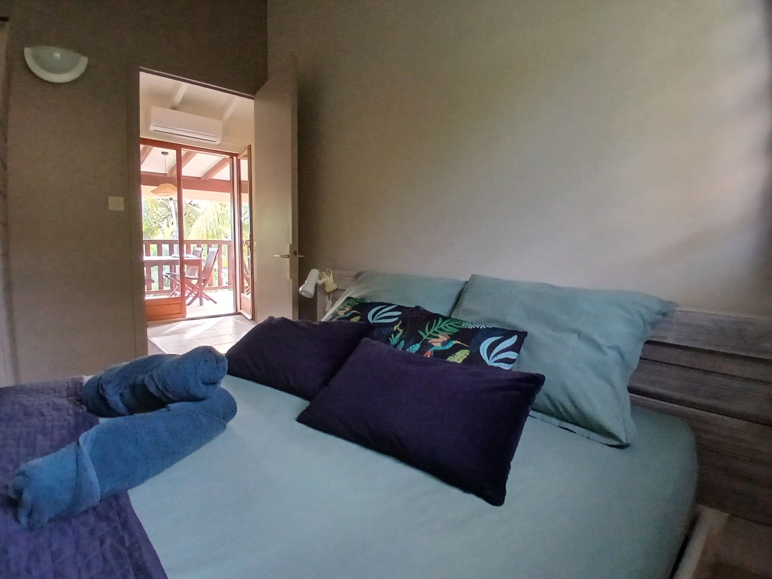 Een slaapkamer met een bed, kussens, een nachtkastje en uitzicht op een buitenruimte.