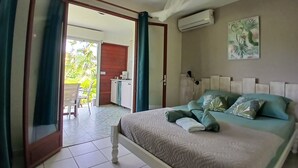 A bedroom with a bed, a desk, a chair, a window with curtains, and a view of the outdoors. - Residence Ti Village Créole (Sainte-Anne)