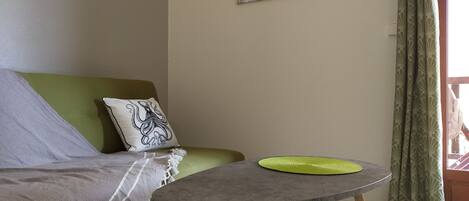 Ein Wohnzimmer mit einem grünen Sofa, einem kleinen Tisch mit grüner Unterlage und einem weißen Kissen mit Motiv eines schwarzen Oktopusses.