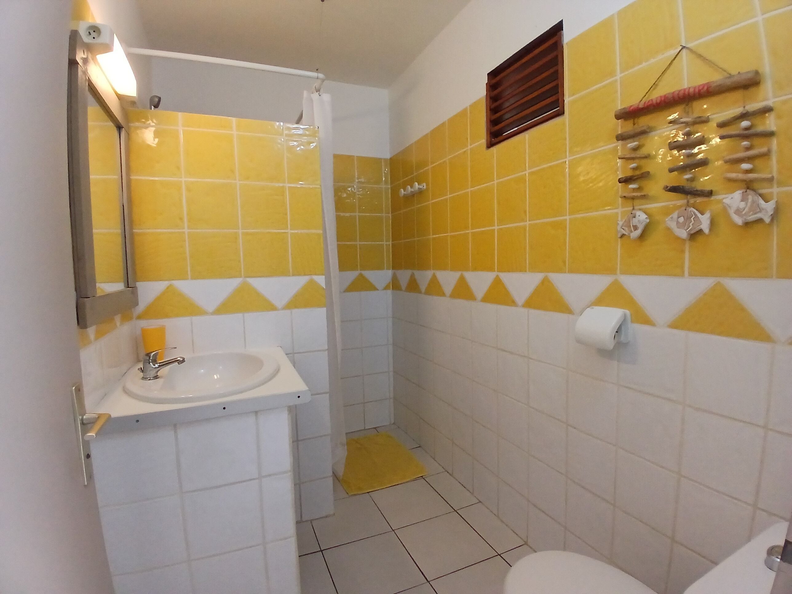 Un baño con azulejos amarillos y blancos, un lavamanos, un inodoro y una zona de ducha.