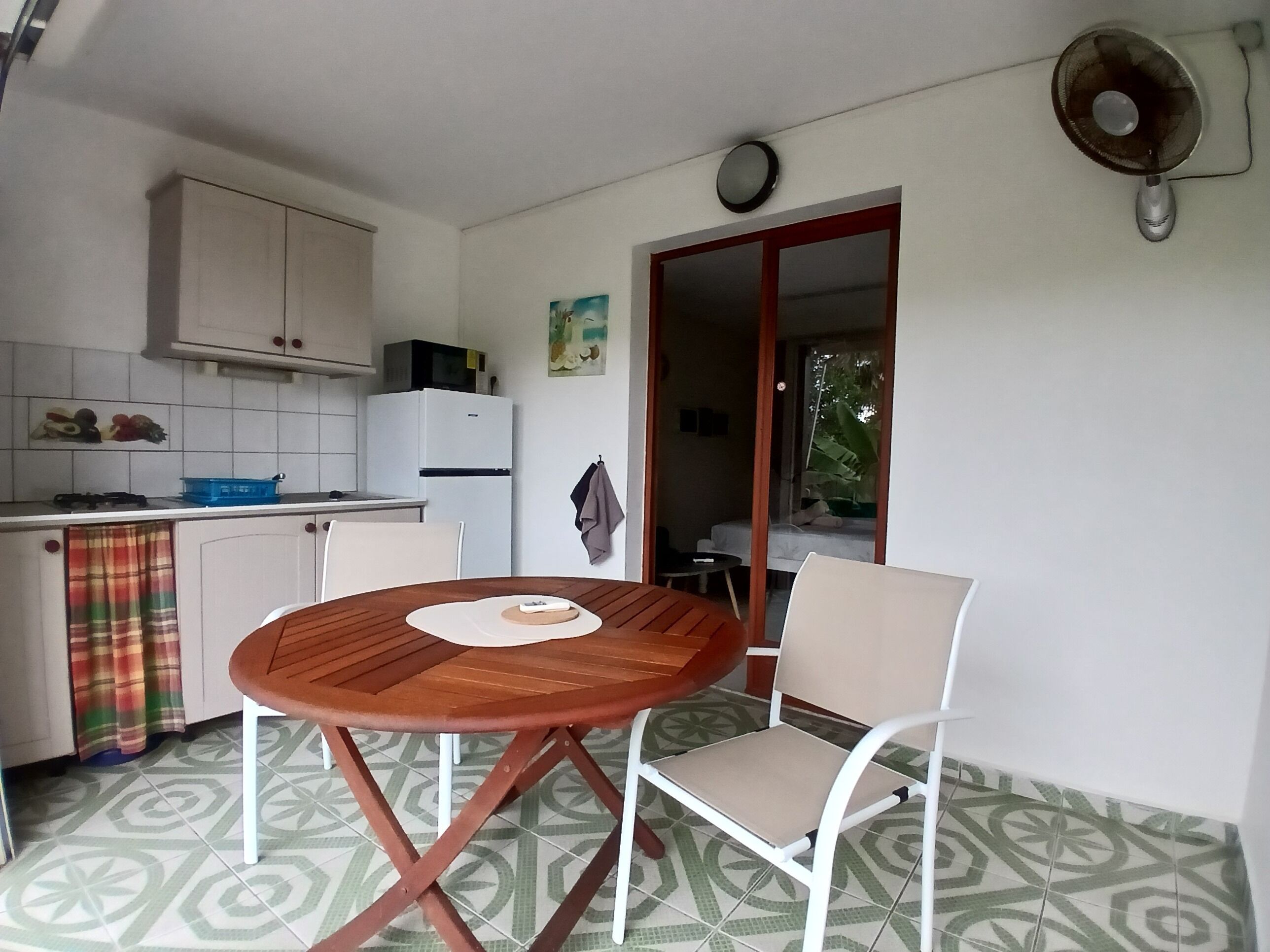 A compact kitchen with white cabinets, a microwave, and a refrigerator. There is a dining area with a wooden table and two chairs.