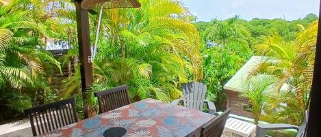 An outdoor patio with a table and chairs, surrounded by lush greenery and a view of the landscape.