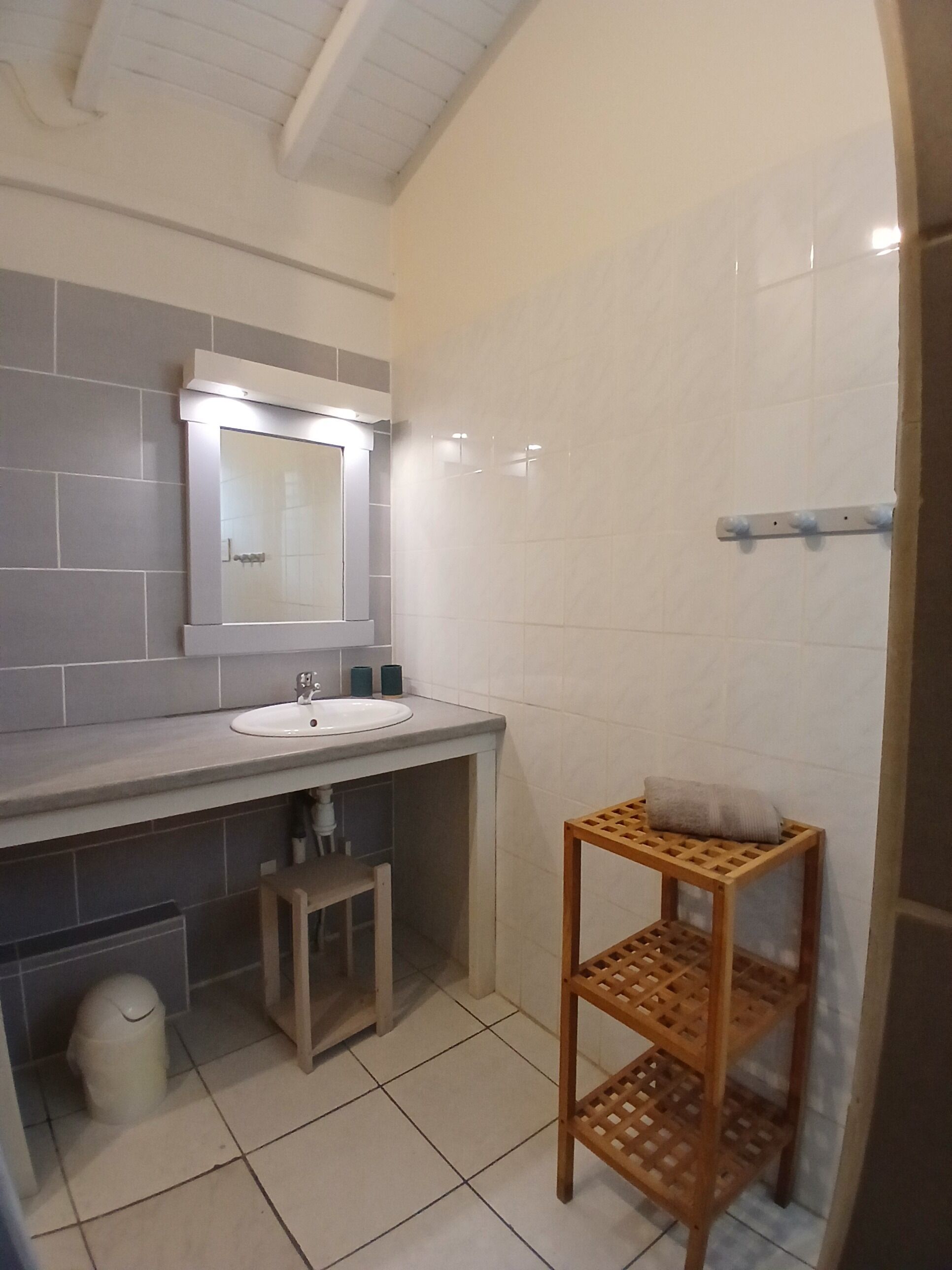 Un baño con lavamanos, espejo, paredes de azulejos y un estante de madera.