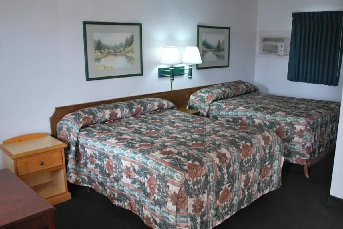 Hotelkamer met twee bedden, een houten nachtkastje, een bureau, twee wandlampen en twee airconditioners.