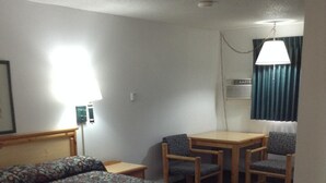 A hotel room with a bed, a desk, and two chairs. - Plaza Inn Great Falls (Great Falls)