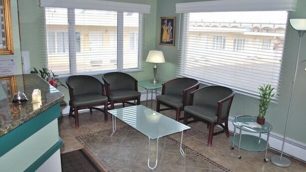A room with a reception desk, two armchairs, a glass table, a lamp, and a potted plant. - Plaza Inn Great Falls (Great Falls)
