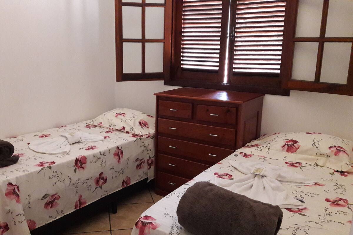 A bedroom with two single beds, a wooden dresser, and a window with blinds.