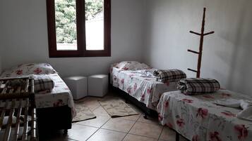 Une petite chambre propre, avec deux lits simples, une chaise en bois, une petite table et une fenêtre donnant sur un paysage verdoyant.