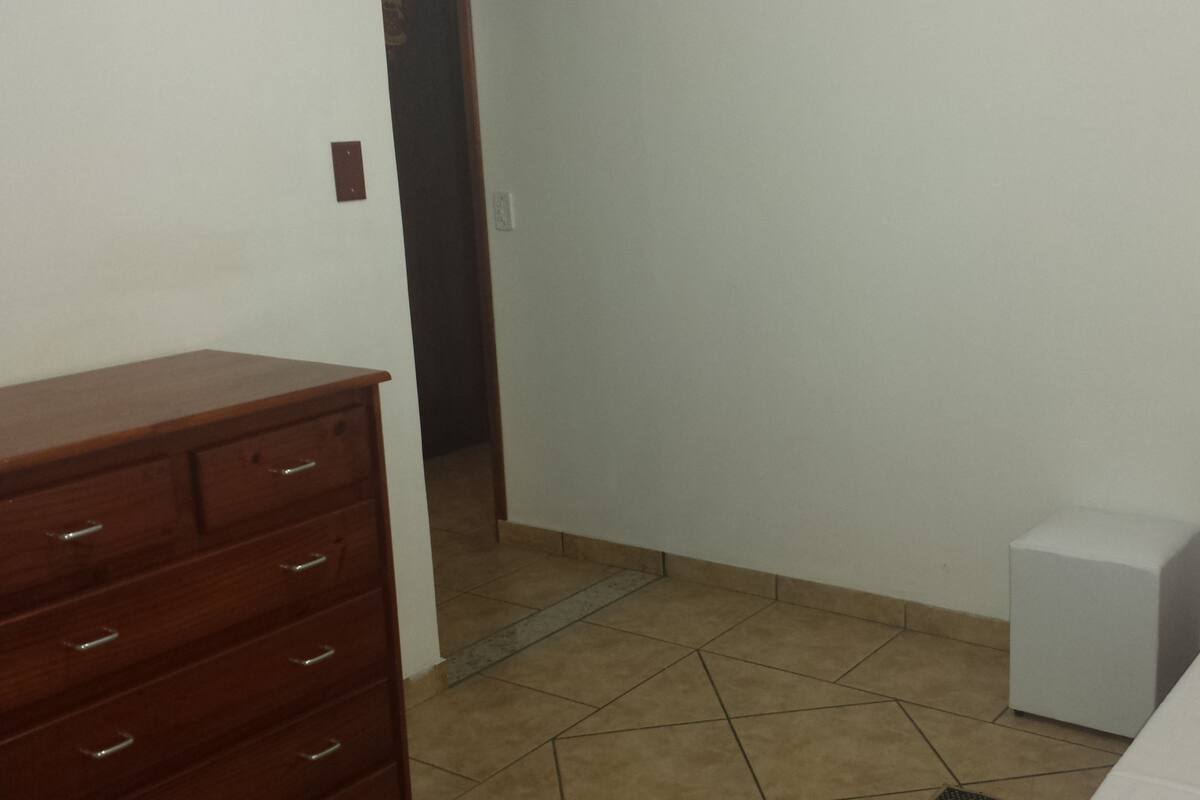 A room with a wooden dresser, a bed, and a small white cabinet.