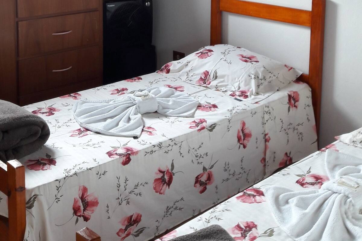 A bedroom with a sloped ceiling, a wooden bed frame, a bedside table, a dresser, and a window.