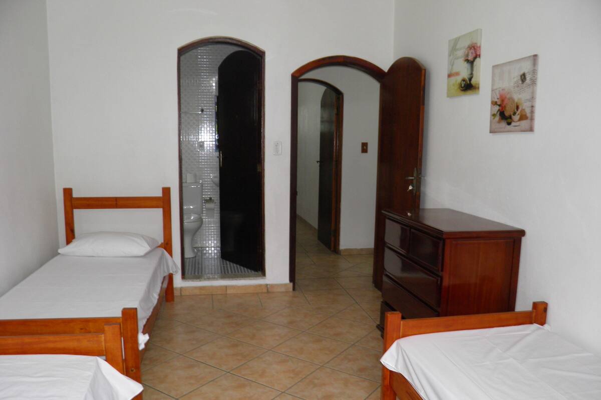A bedroom with two wooden beds, a wooden dresser, and a bathroom visible through an archway.