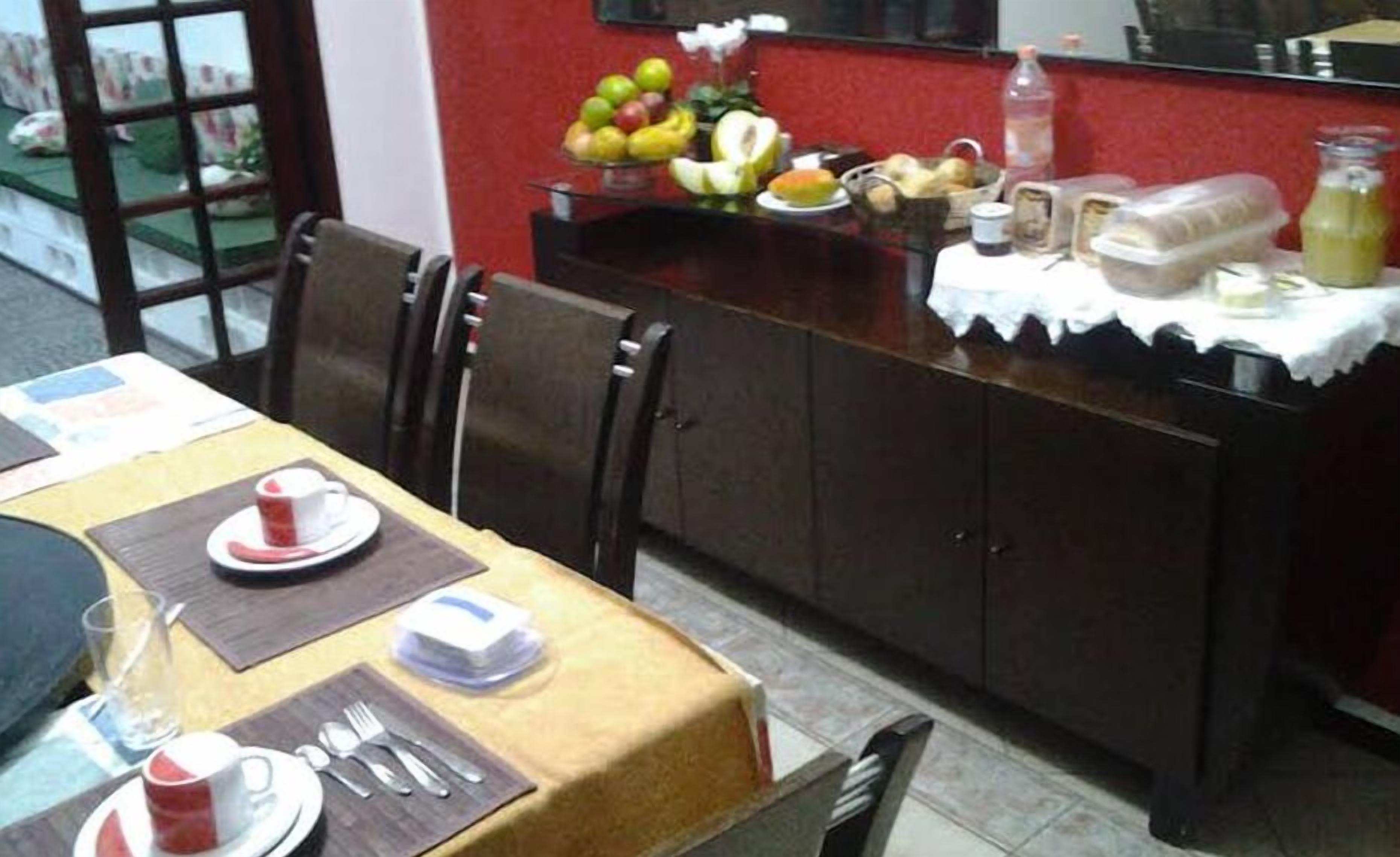 A dining area with a table set for two, a fruit display, and a refrigerator in the background.