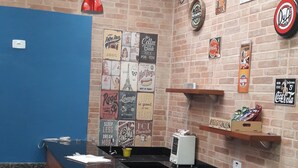 A counter area with a black marble top, red pendant lights, and a brick wall with various posters and signs. - Pousada Sognares (Guarulhos)
