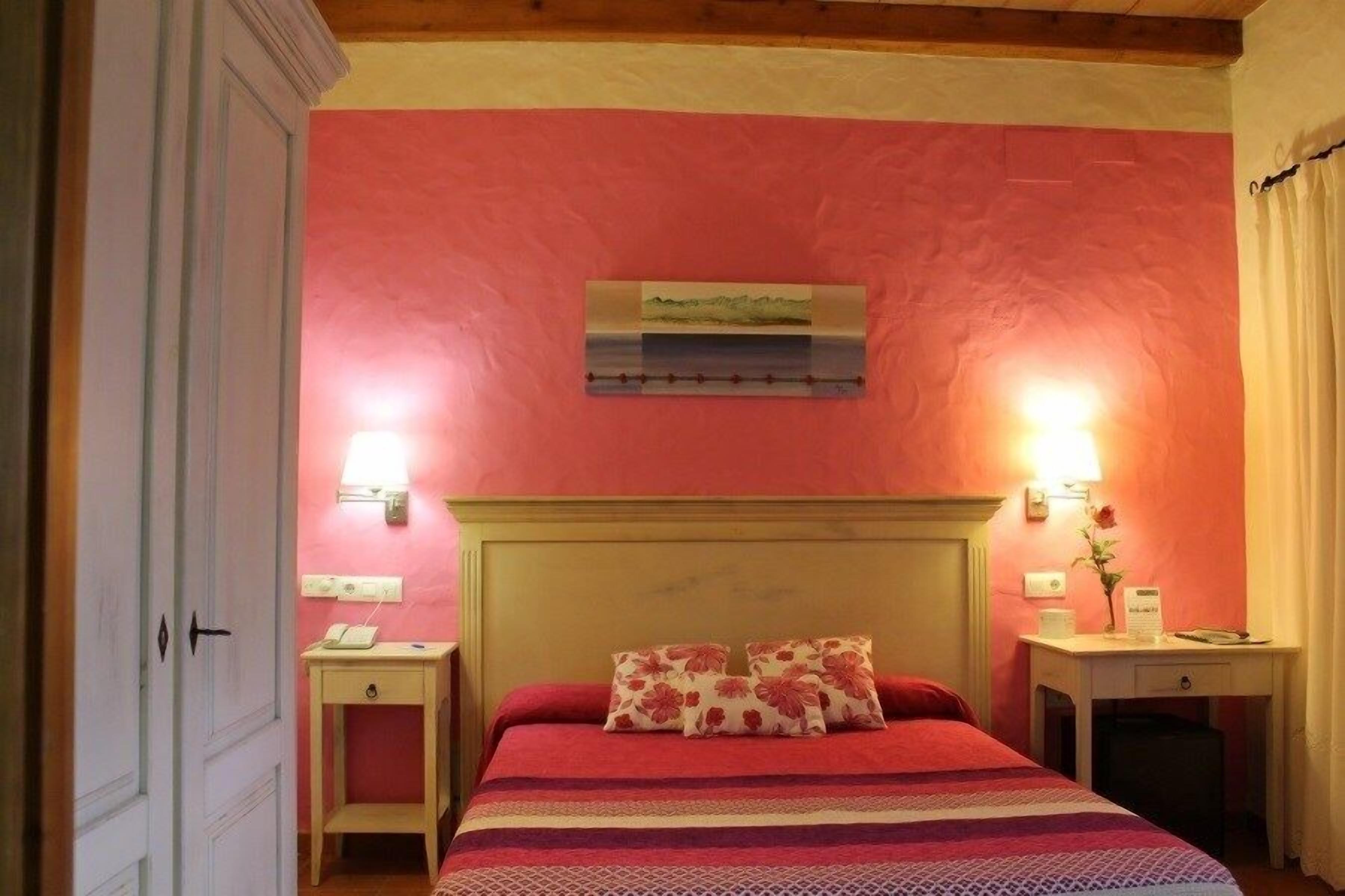 Un dormitorio con cama, mesitas de noche, lámpara de pared y un cuadro.