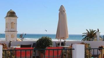Una terraza frente al mar con sillas rojas, un edificio blanco con cúpula y vistas a la playa.