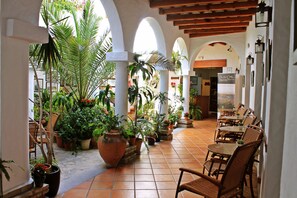 Un patio couvert doté d’un sol carrelé, de plantes en pot et de meubles en osier.
