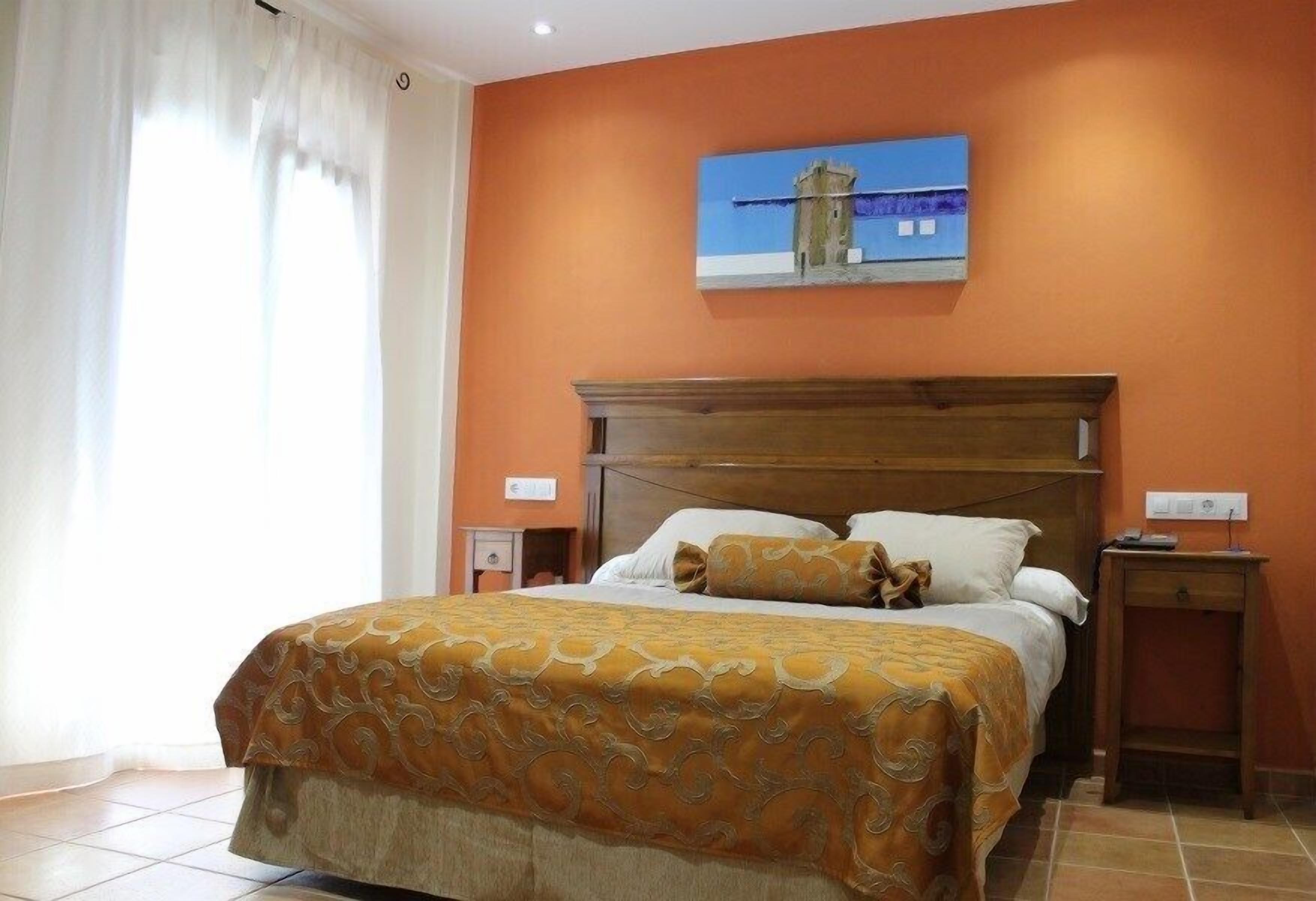 A hotel room with a large bed, a wooden headboard, a painting on the wall, and a nightstand.