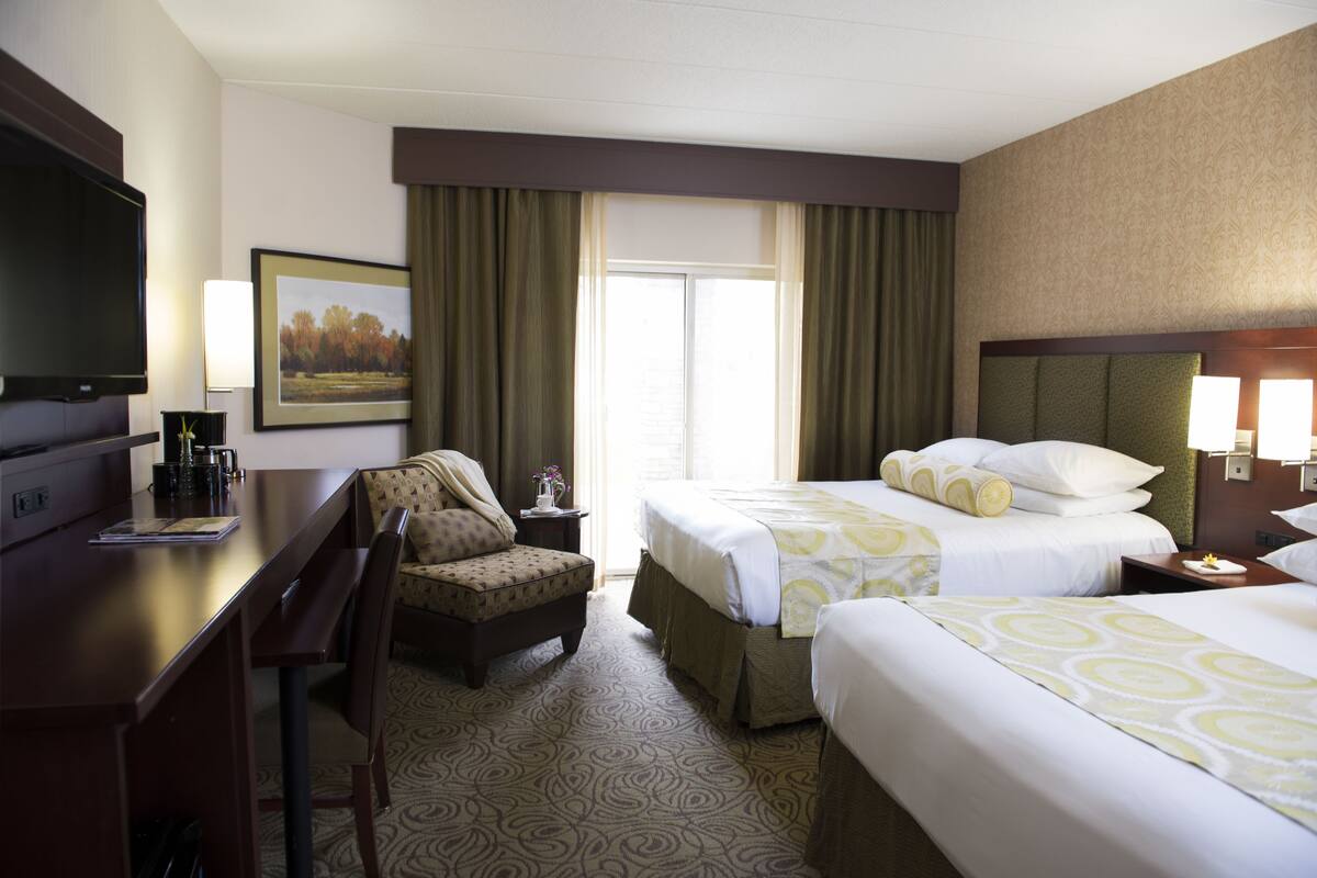 Hotelkamer met twee bedden, een bureau, een stoel, een televisie en een raam met gordijnen.