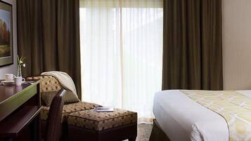 A hotel room with a bed, a desk, a chair, and a window with curtains.