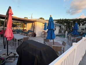 An outdoor patio area with tables and chairs, a barbecue grill, and umbrellas. - Pelican By The Sea (Pompano Beach)