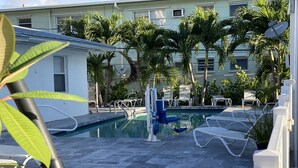 A pool area with lounge chairs, a water fountain, and palm trees. - Pelican By The Sea (Pompano Beach)