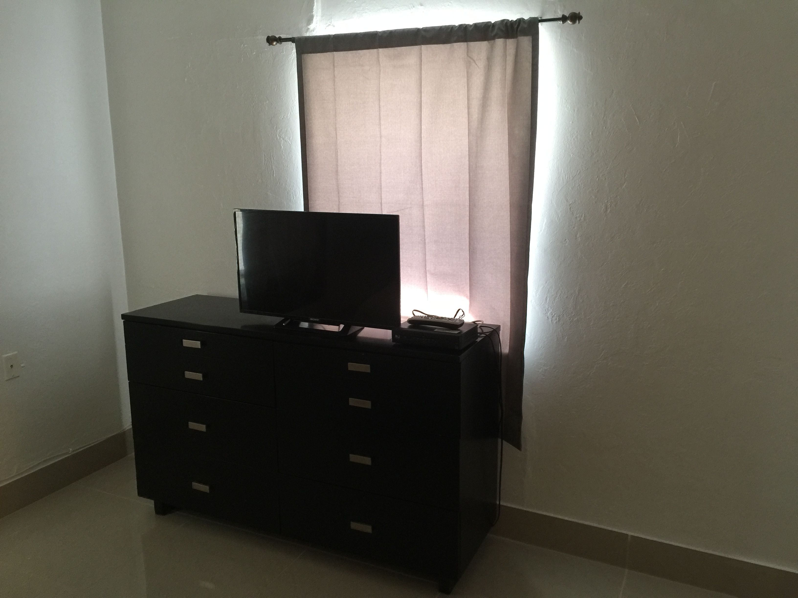 Un televisor negro sobre un aparador en una habitación con ventana y cortinas.