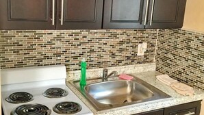 A kitchen with dark cabinets, a white stove, a stainless steel sink, and a mosaic backsplash. - Pelican By The Sea (Pompano Beach)