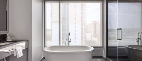 A modern bathroom with a freestanding bathtub, a glass shower enclosure, and a large window offering a city view.