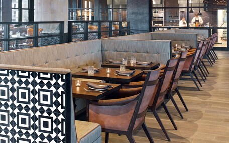 A restaurant with a modern interior, featuring wooden ceiling beams and a long dining area with booths and tables.