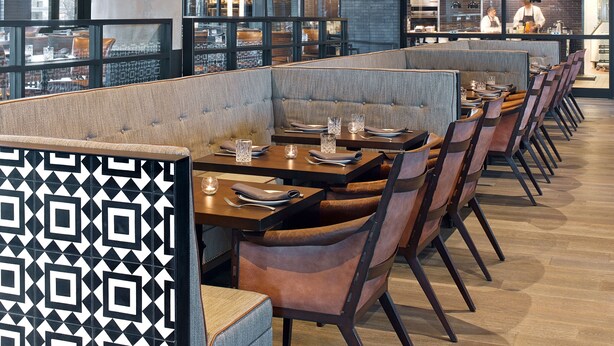 Un restaurante con una decoración moderna, que presenta vigas de madera en el techo y una amplia zona de comedor con cabinas y mesas.