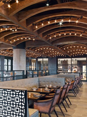A restaurant with a modern interior, featuring wooden ceiling beams and a long dining area with booths and tables. - Hotel Van Zandt (Austin)