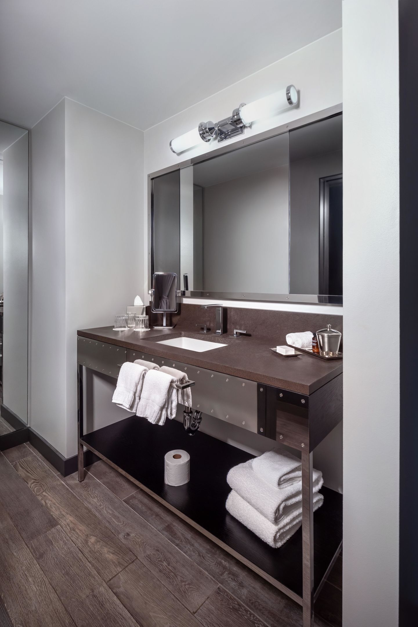 A modern bathroom with a dark countertop, two sinks, a large mirror, and a towel rack.