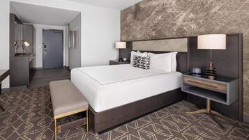 A modern hotel room with a large bed, bedside tables, a bench, and a textured wall.