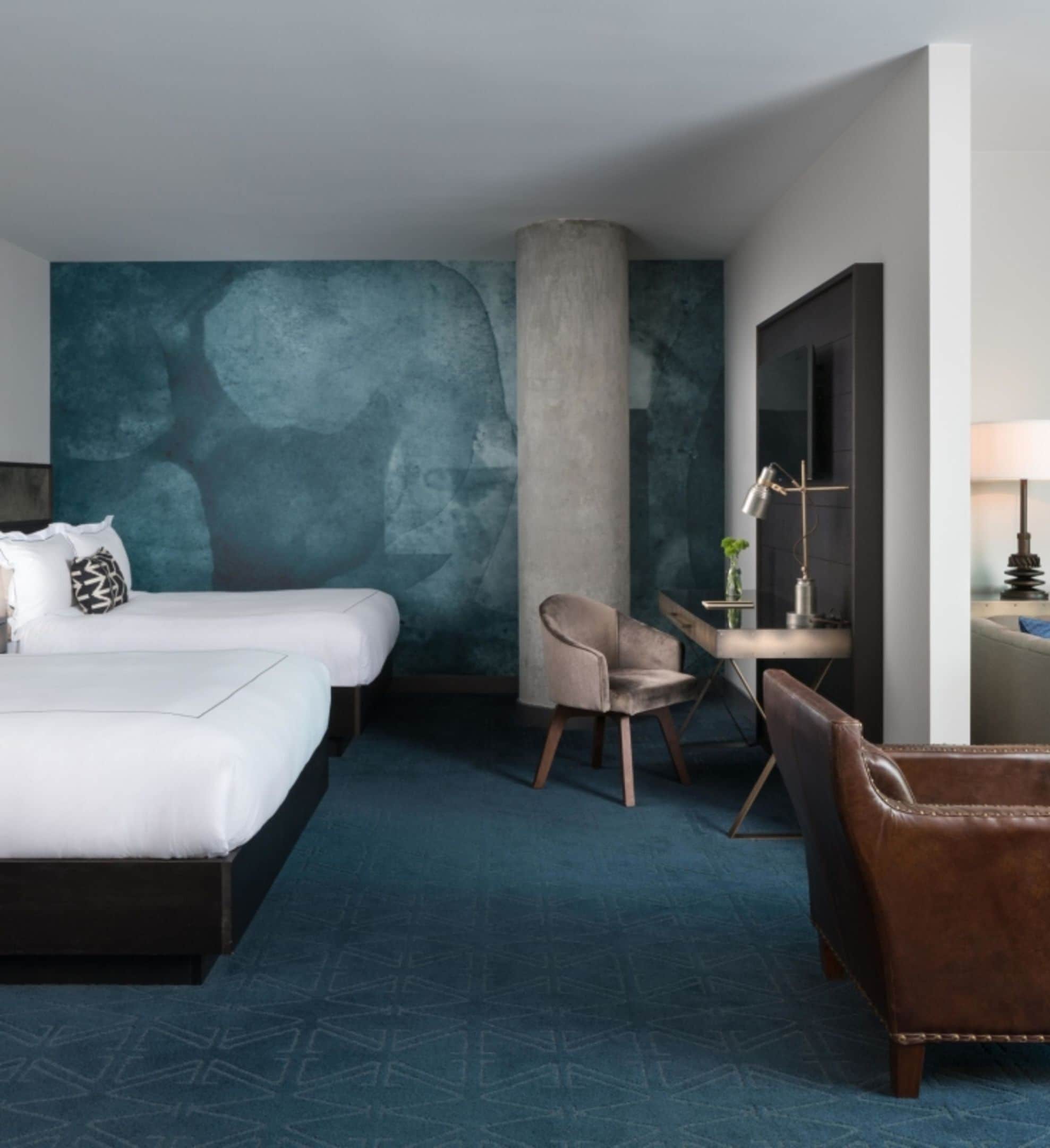 Habitación de hotel con dos camas, un escritorio, una silla y un gran mural abstracto en la pared.
