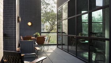 Un área de estar al aire libre con mesas y sillas, una planta en maceta y vistas a árboles a través de amplias ventanas.