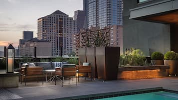 A rooftop pool area with seating, a planter with plants, and a city skyline in the background.