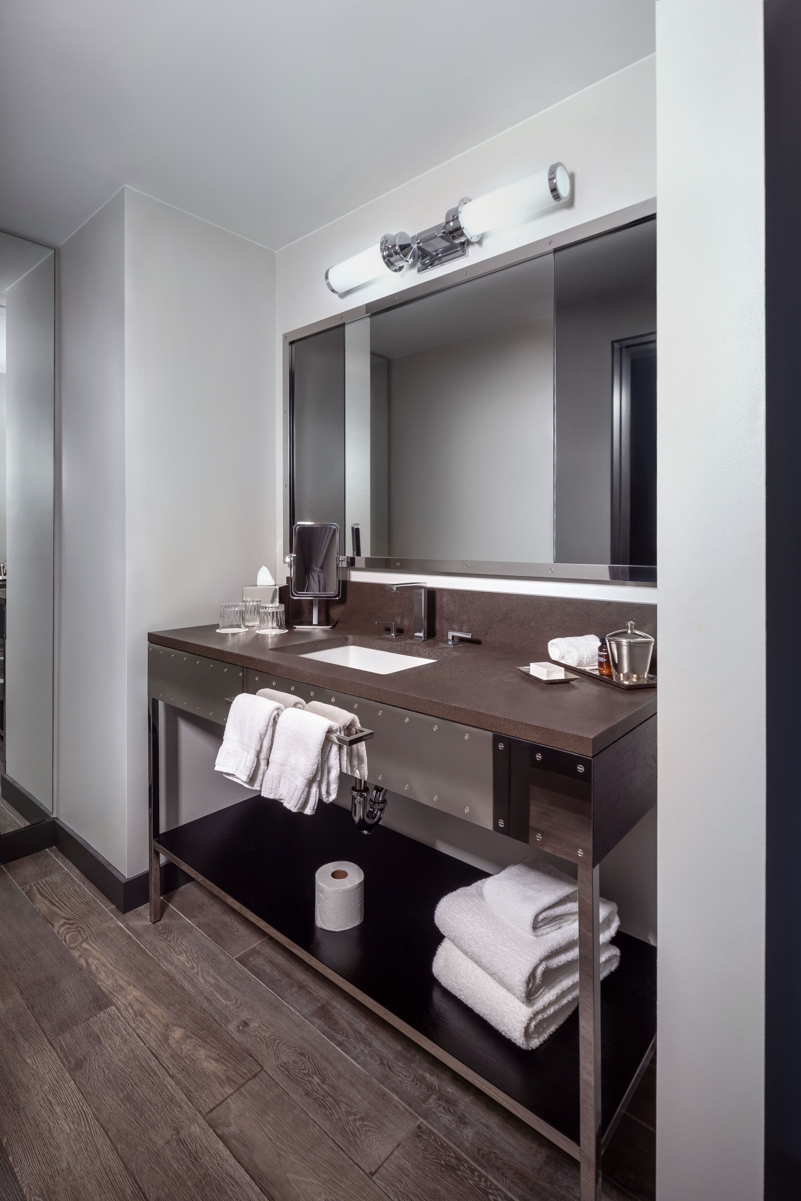 A modern bathroom with a dark countertop, a large mirror, a sink, and a towel rack.
