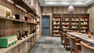 Um quarto com paredes de madeira, uma mesa comprida com cadeiras e uma estante repleta de livros.