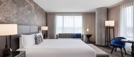 A hotel room with a large bed, a sofa, a desk, a chair, and a lamp.
