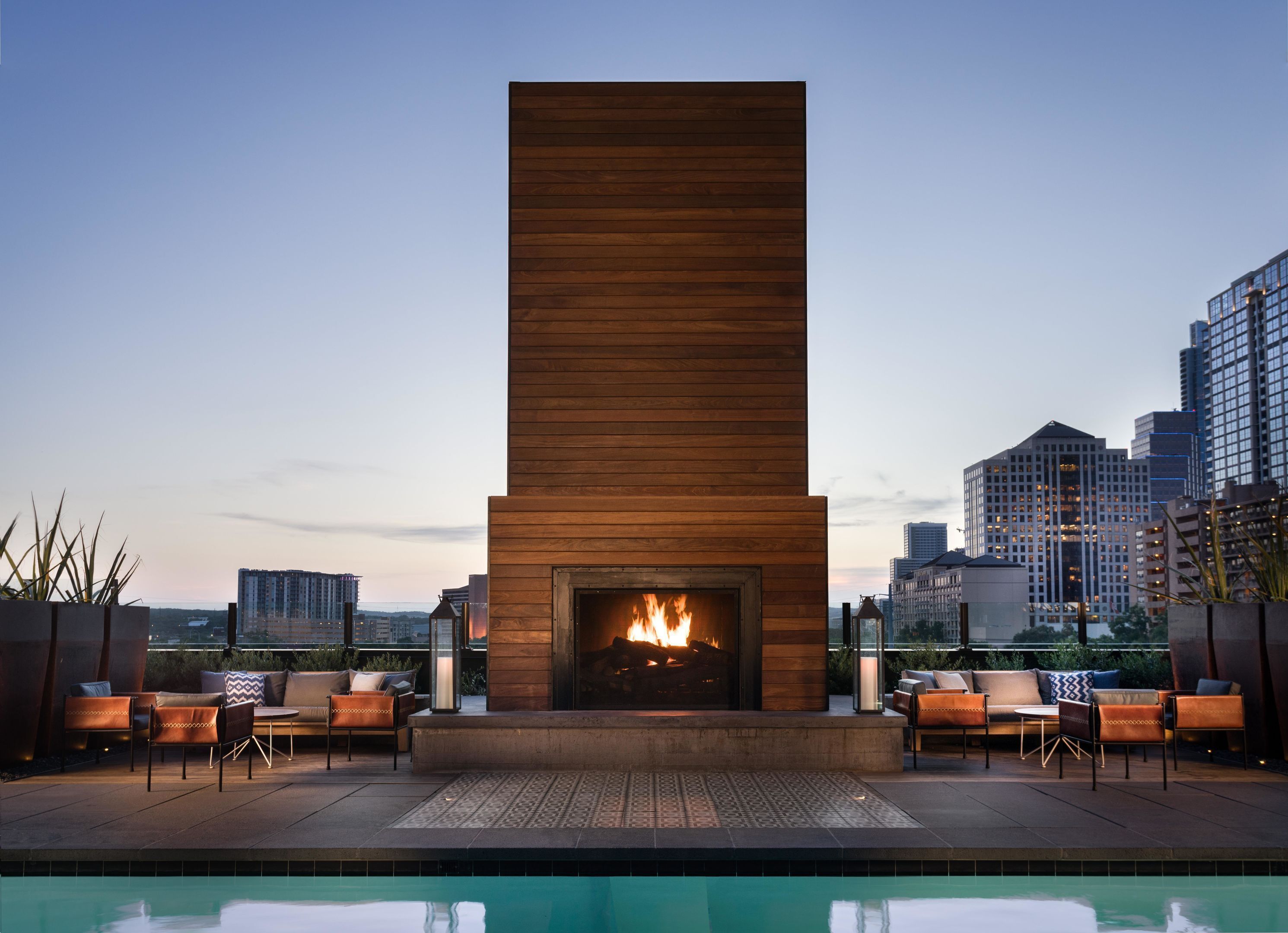 Uma área de piscina no terraço com lareira moderna, cadeiras de descanso e vista para o horizonte da cidade.