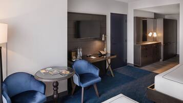 A hotel room with a desk, two chairs, a television, a mirror, and a bed.