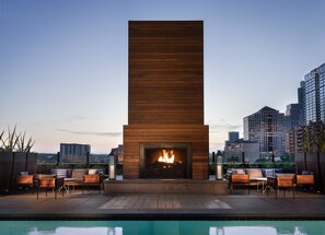 A rooftop pool area with a modern fireplace, lounge chairs, and a city skyline in the background. - Hotel Van Zandt (Austin)