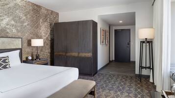 A hotel room with a bed, bench, nightstand, lamp, wardrobe, and patterned floor.